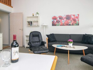 A modern living room with a leather armchair, a grey sofa, a white coffee table, and a bookshelf with books and decorative items. - 8 Person Holiday Home in Ringkobing (Ringkobing)