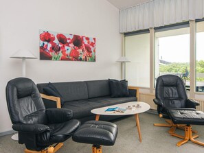 A modern living room with a grey sofa, two black leather chairs, a small white coffee table, and a painting of red flowers on the wall. - 8 Person Holiday Home in Ringkobing (Ringkobing)