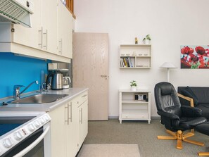 A compact living space with a kitchenette, a black leather chair, and a bookshelf with decorative items. - 8 Person Holiday Home in Ringkobing (Ringkobing)