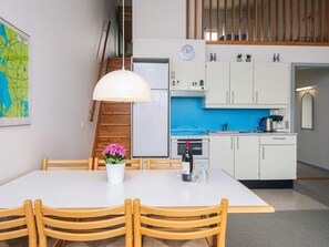 Cocina compacta con armarios blancos, salpicadero azul y un comedor con mesa blanca y sillas de madera.