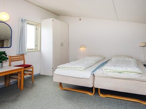 Quarto pequeno e limpo com escrivaninha, duas camas de solteiro, guarda-roupa e janela com cortinas.