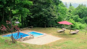 A backyard with a swimming pool, two lounge chairs, and a red umbrella.