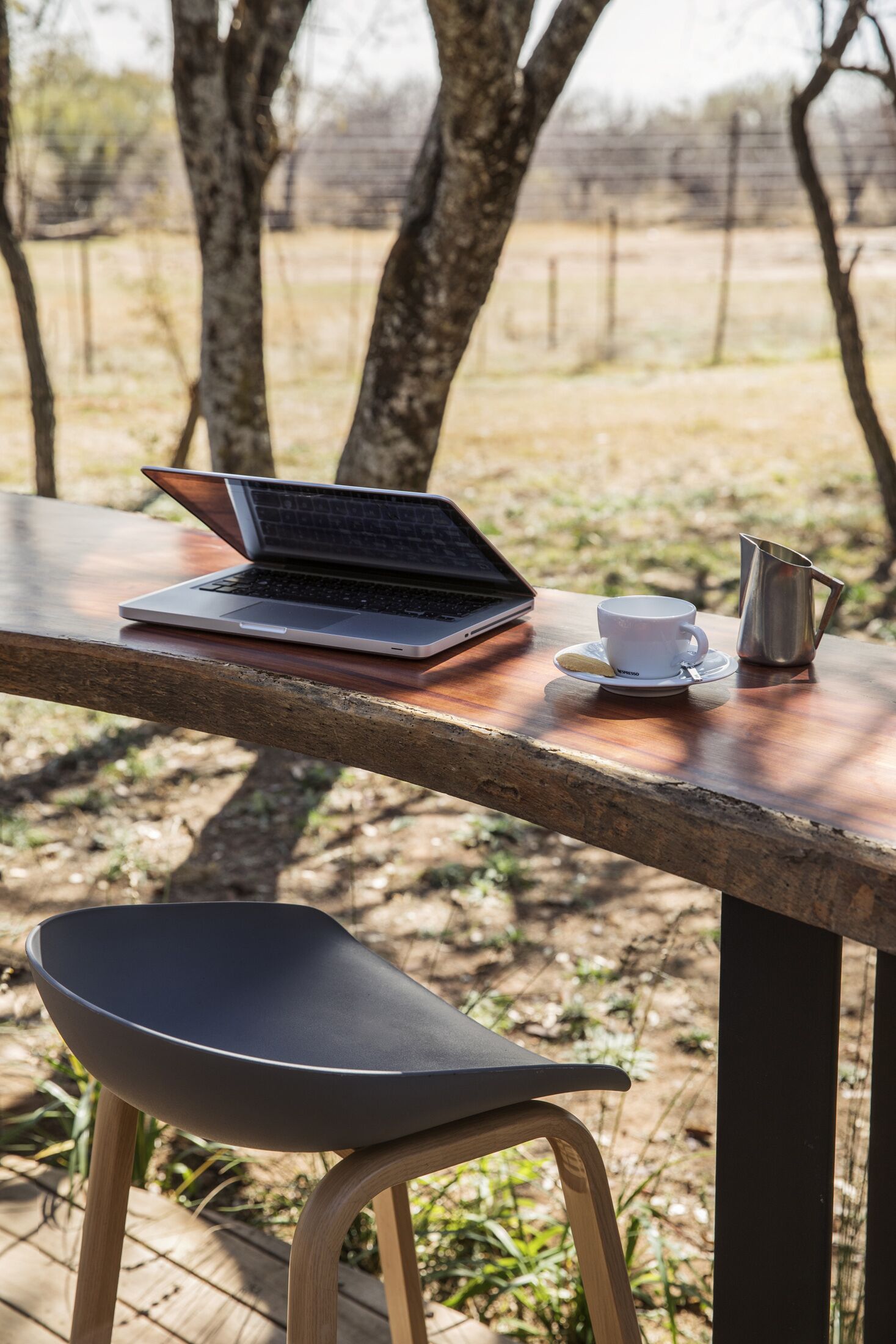 A laptop on a wooden table with a white cup and a metal pitcher.