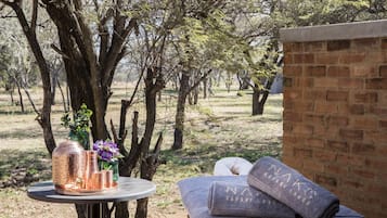 Relax in a serene outdoor setting surrounded by trees and a brick wall, with a cozy bench and a beautifully set table.