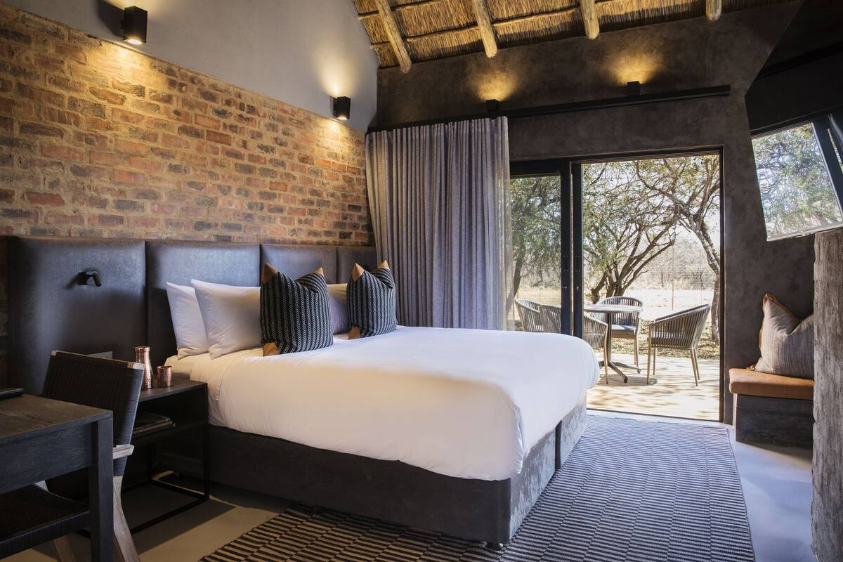 A modern bedroom with a large bed, a brick wall, and a view of the outdoors.