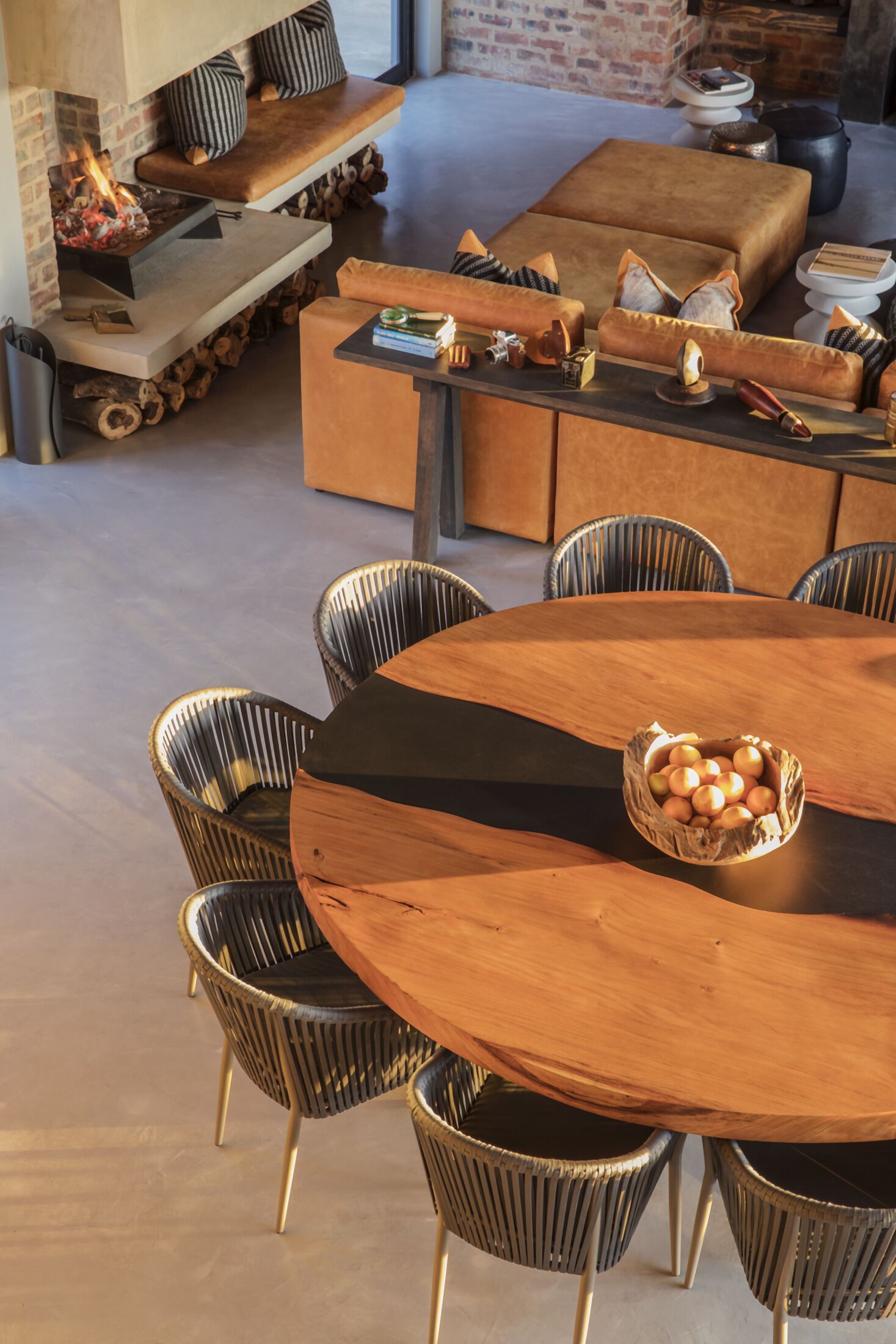 A modern dining area with a round wooden table, black and gold chairs, and a woven basket of apples.
