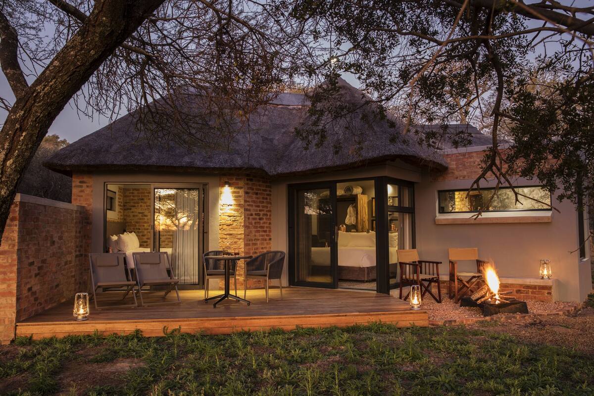 A modern house with a thatched roof, a glass door entrance, and a patio with outdoor seating and a fire pit.