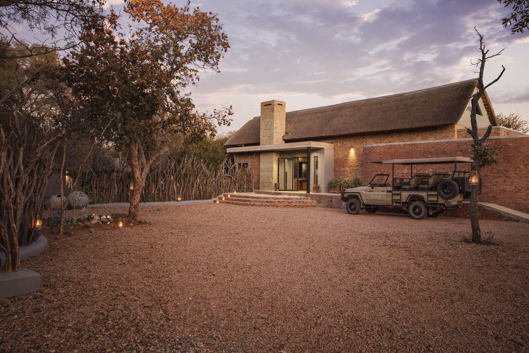 A house with a gravel driveway, a jeep, and a thatched roof.
