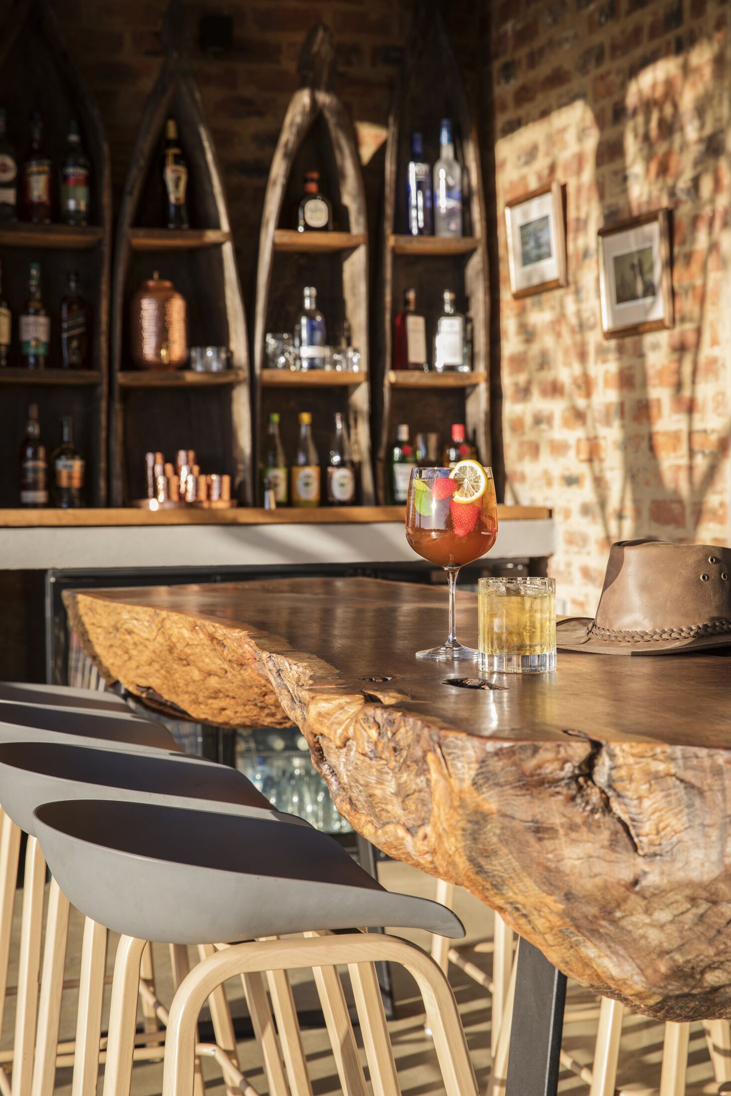 Un espace bar avec une table en bois rustique, des tabourets de bar et des étagères remplies de bouteilles.