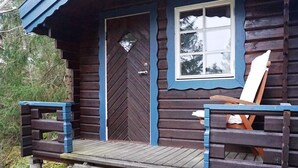 Eine Holzhütte mit einer Haustür, einem Fenster und einer Veranda mit einer Bank.