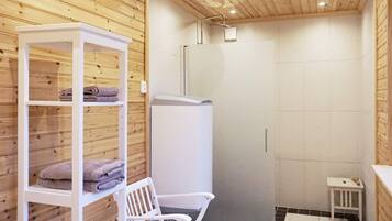 A bathroom with wooden paneling, a white bench, a shelf with towels, and a shower area.