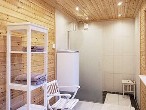 A bathroom with wooden paneling, a white bench, a shelf with towels, and a shower area. - 4 Star Holiday Home in Ingaro (Ingaro)