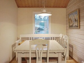A dining area with a white table and chairs, a hanging light fixture, a window with a view of snow-covered ground, and a framed picture on the wall.