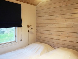 Una habitación con una cama, una ventana con cortina negra y una lámpara de pared.