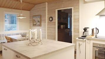 A kitchen with a central island, wooden walls, a dining area with a table and chairs, and a view through an open door.