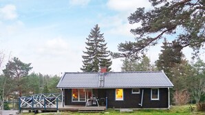 Eine kleine, dunkel gefärbte Holzhütte mit einem Ziegeldach, einer Veranda und einer kleinen Terrasse.