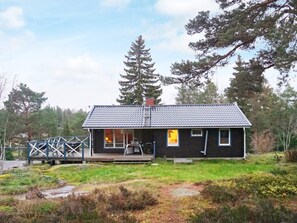 A small, dark-colored cabin with a tiled roof, a porch, and a small deck. - 4 Star Holiday Home in Ingaro (Ingaro)