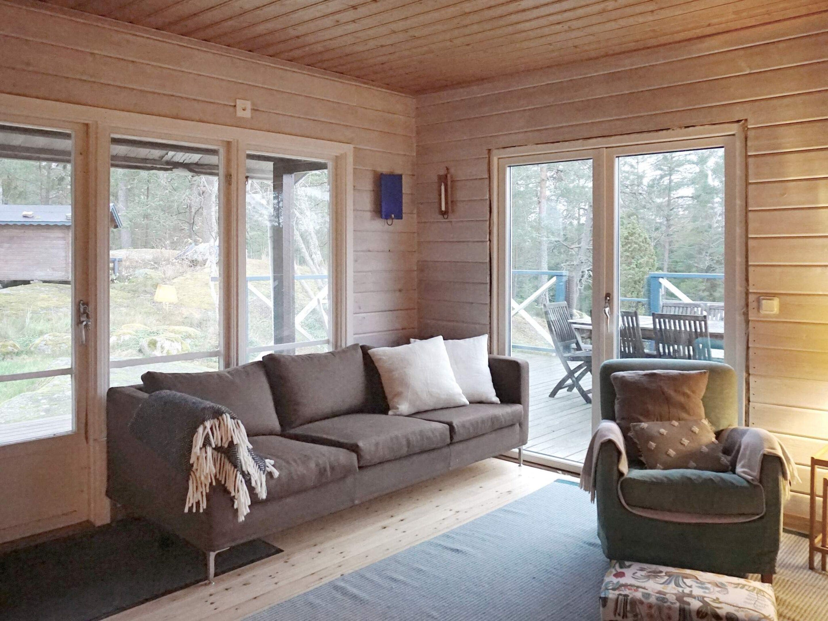 Un cuarto acogedor con techo de madera, un sofá gris, un sillón verde y un amplio ventanal corredera que da a una terraza exterior.