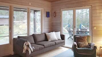 Un cuarto acogedor con techo de madera, un sofá gris, un sillón verde y un amplio ventanal corredera que da a una terraza exterior.