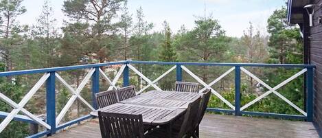 Une terrasse en bois avec une table et des chaises, entourée d’une rambarde bleue.