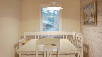 A dining area with a white table and chairs, a hanging light fixture, a window with a view of snow-covered ground, and a framed picture on the wall.