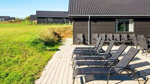 A modern building with a flat roof, outdoor seating area with metal chairs, and a grassy field in the background. - 5 Star Holiday Home in Sydals (Sydals)