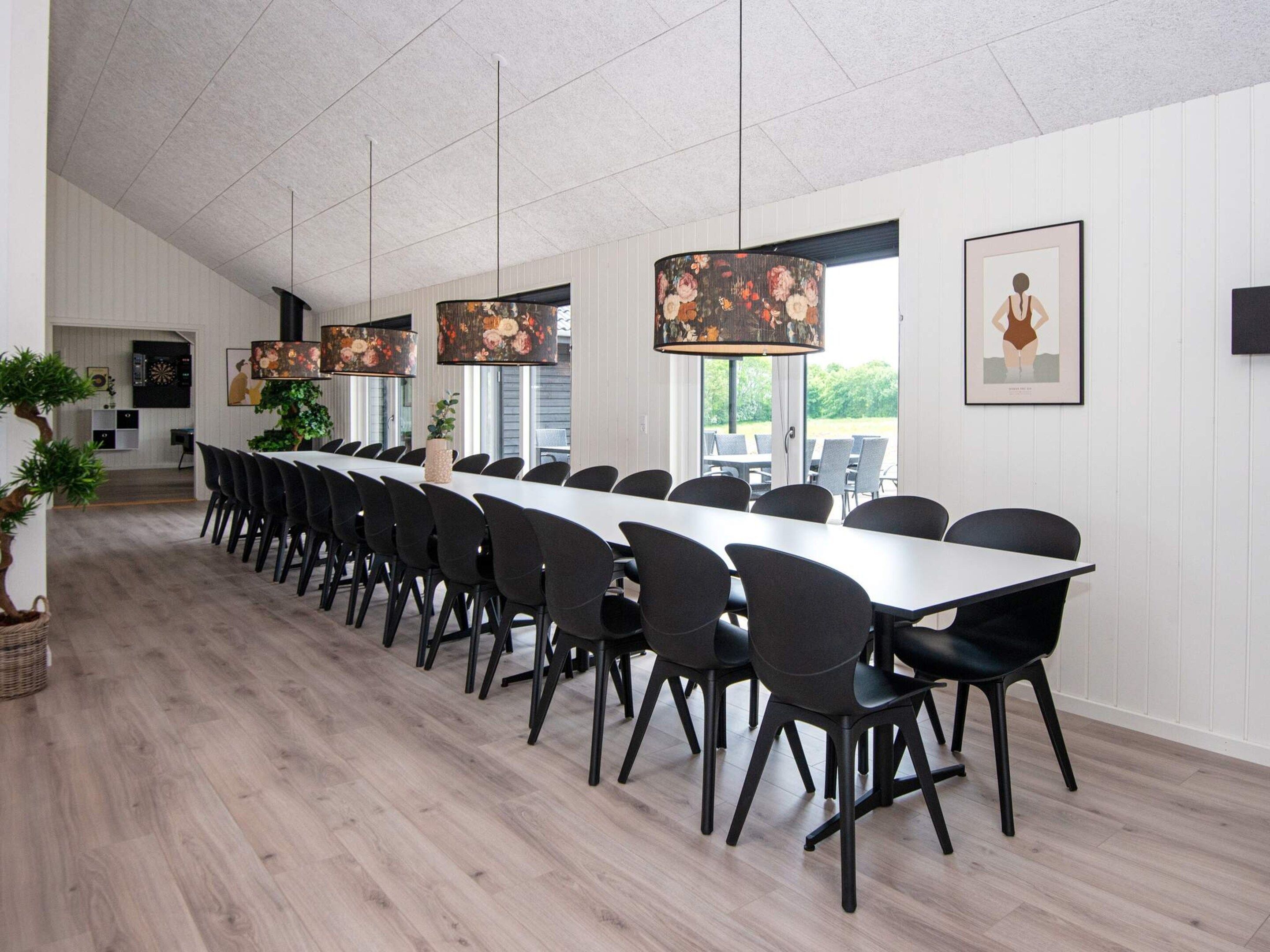 Ein langer Esstisch mit Stühlen, eine hängende Blumenleuchte und ein gerahmtes Kunstwerk an der Wand.