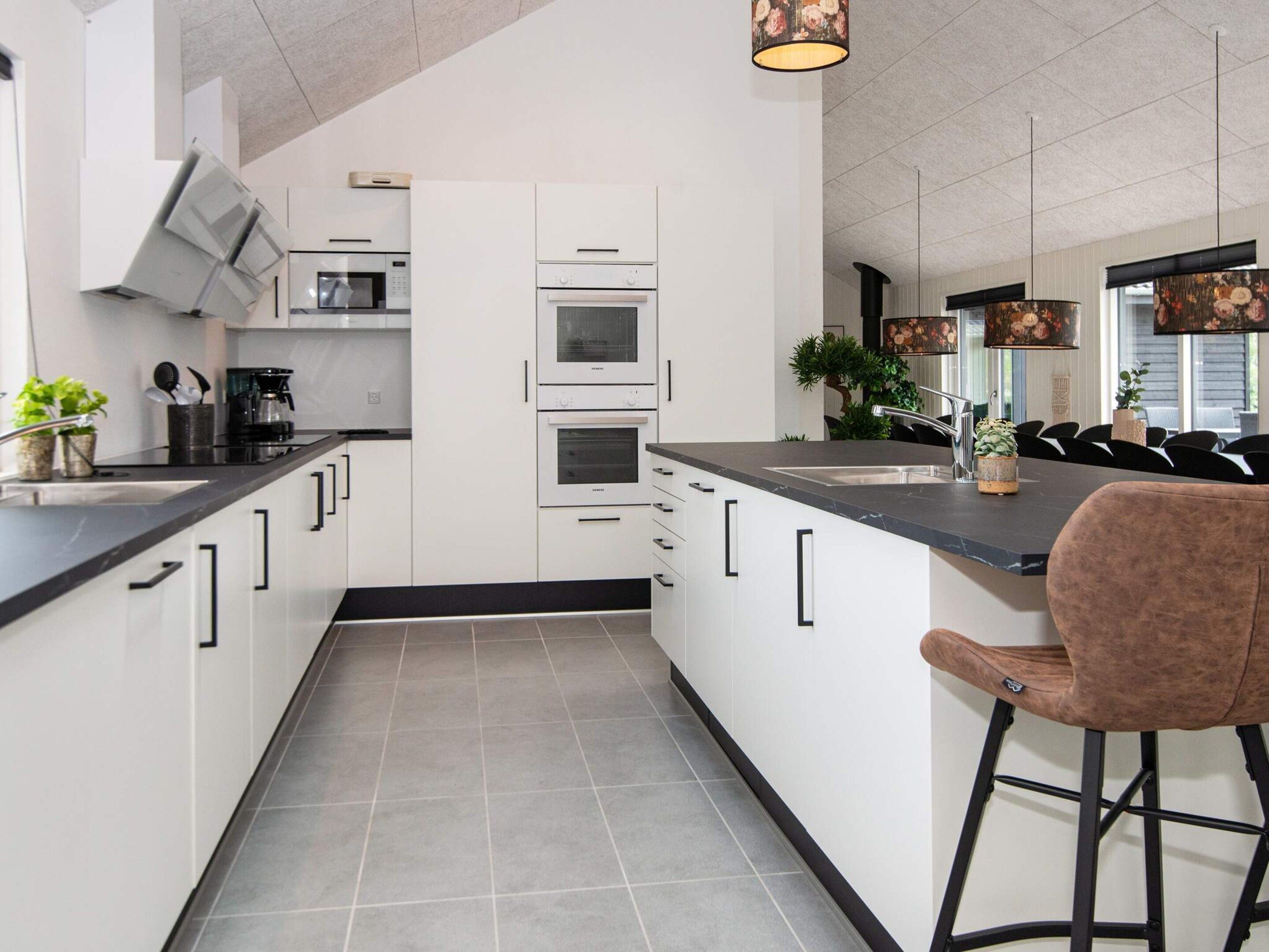 A modern kitchen with white cabinetry, a black countertop, and a bar stool.