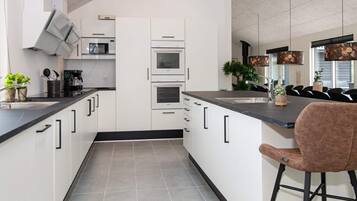 A modern kitchen with white cabinetry, a black countertop, and a bar stool.