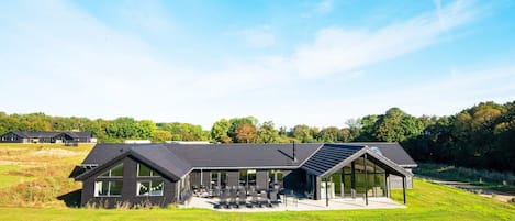 A modern house with a large patio area, a swimming pool, and a view of the surrounding landscape.