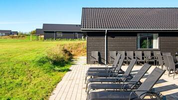 Een modern gebouw met een plat dak en een verhard terras met ligbedden.