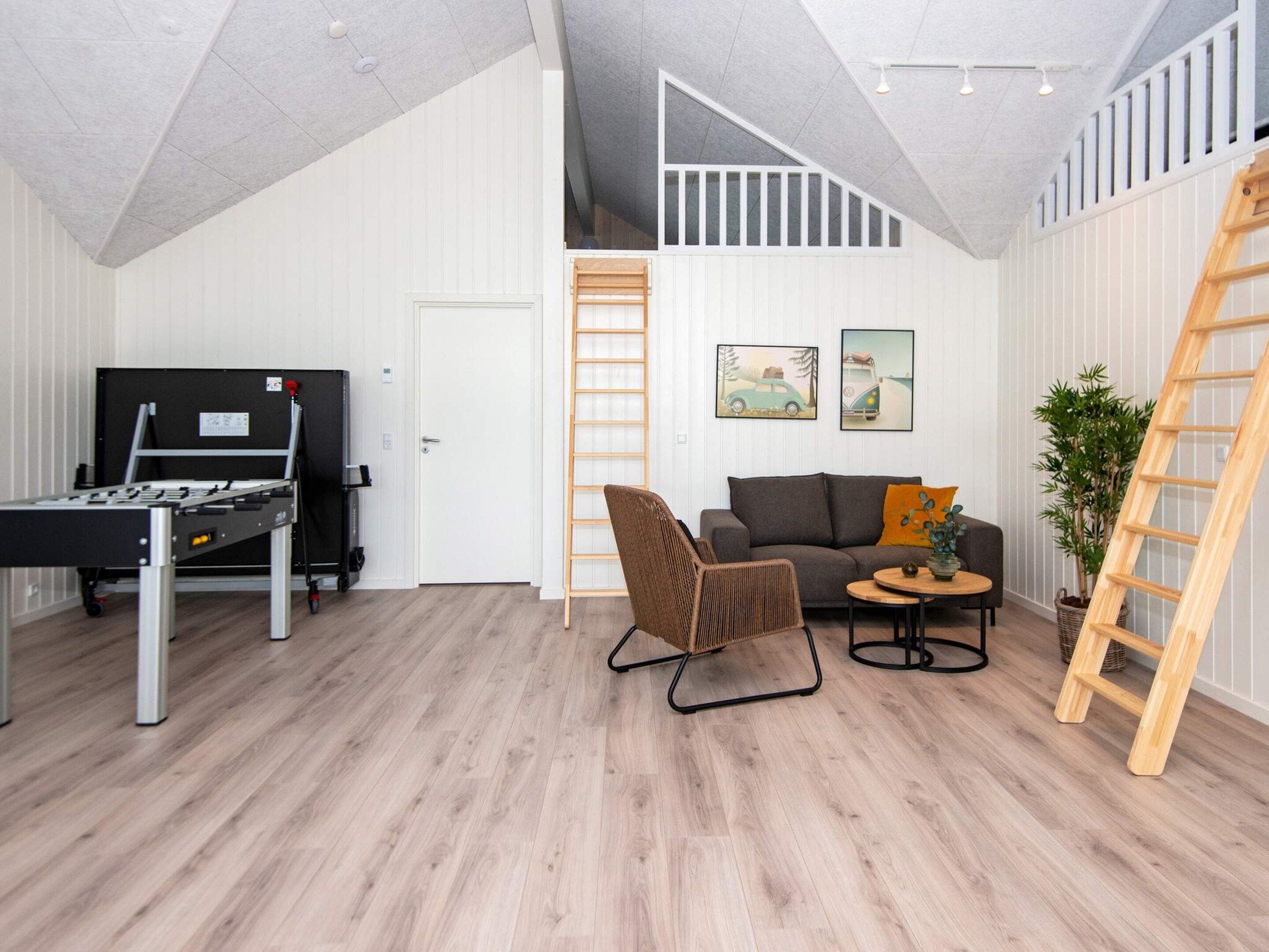 A room with a foosball table, a sofa, a coffee table, and a ladder.