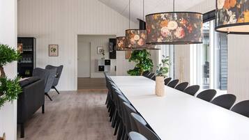 A modern dining area with a long table, black chairs, and a floral-patterned hanging light fixture.