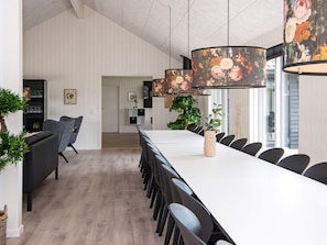 Een moderne eetruimte met een lange tafel, zwarte stoelen en een hanglamp met bloemenprint.