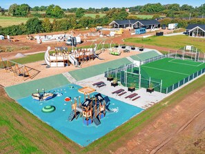 Eine Vogelperspektive auf einen Spielplatz mit verschiedenen Spielgeräten, einem kleinen Schwimmbecken und einem Sportplatz.