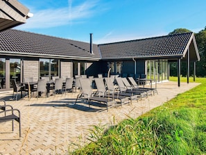 Een moderne patio buiten met lounge fauteuils en tafels, een overdekte zithoek en een pad van baksteen.