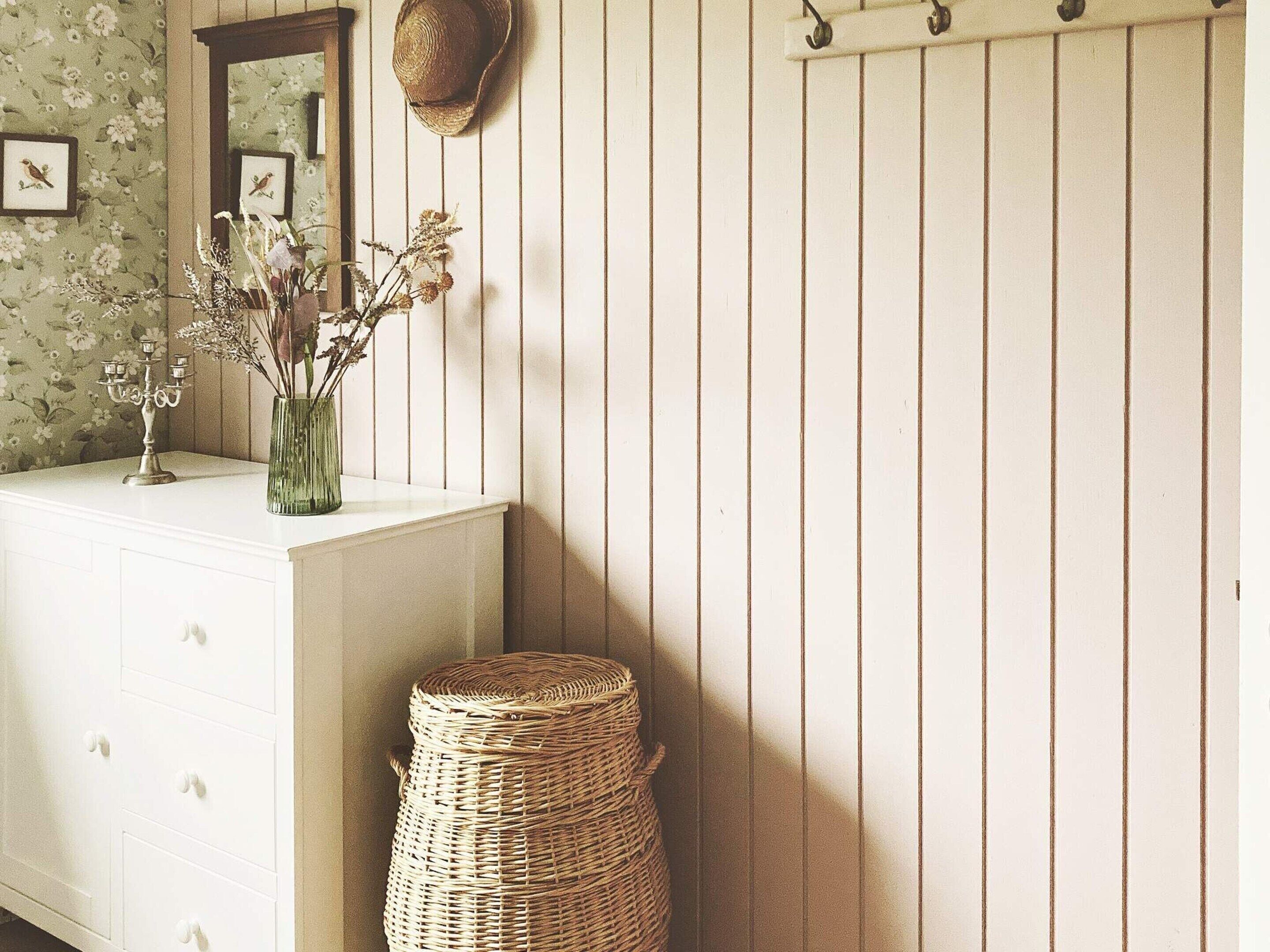 A room with a white dresser, a wicker basket, a mirror, and a wall with vertical lines.