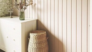 A room with a white dresser, a wicker basket, a mirror, and a wall with vertical lines. - 6 Person Holiday Home in Augustenborg (Augustenborg)