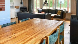 A cozy living room with a wooden dining table, a black leather sofa, and a black armchair. There is a black heater on the right and a window with a view of greenery outside. - 6 Person Holiday Home in Augustenborg (Augustenborg)