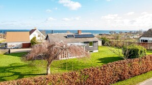 A coastal residential area with houses, a grassy lawn, and a view of the sea. - 6 Person Holiday Home in Augustenborg (Augustenborg)