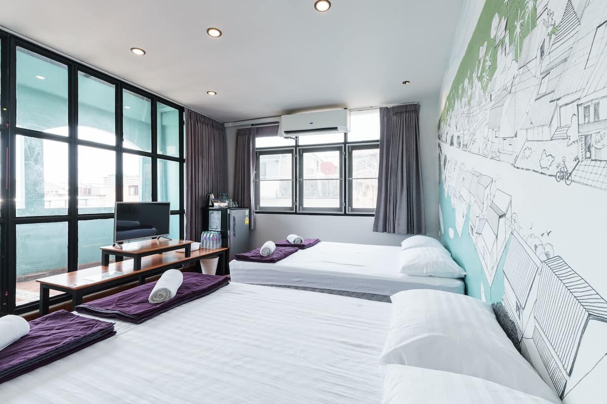 A hotel room with two beds, a desk, a TV, and large windows.
