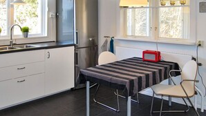 Une cuisine moderne avec un réfrigérateur en acier inoxydable, une table à manger recouverte d’une nappe à rayures et une chaise.