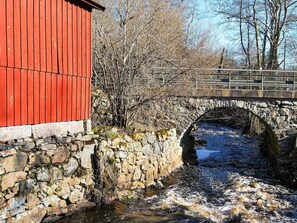 Kivinen silta virran yllä, punainen rakennus ja kivimuuri.