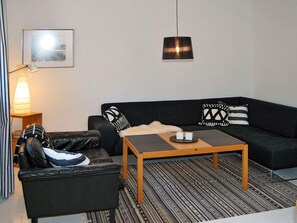 A modern living room with a black leather sofa, a wooden coffee table, and a patterned rug. - 4 Star Holiday Home in Vittsjo (Vittsjo)