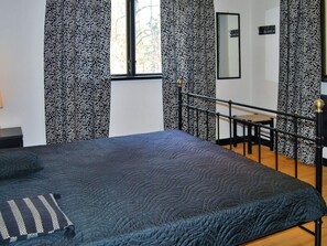 A bedroom with a bed, a window, a mirror, and patterned curtains.