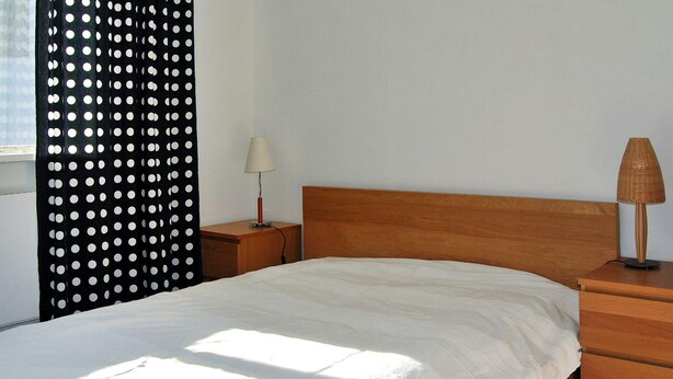 Une chambre avec un lit en bois, une table de chevet avec une lampe, un rideau à pois noirs et blancs et une fenêtre.