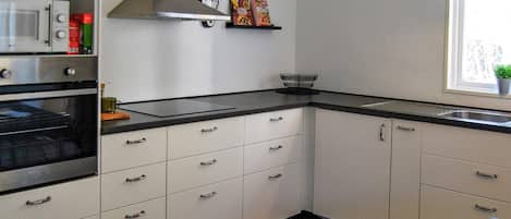 A kitchen with white cabinets, a black countertop, a stainless steel range hood, a microwave, and a clock on the wall.