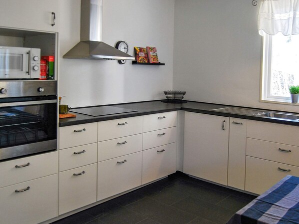 A kitchen with white cabinets, a black countertop, a stainless steel range hood, a microwave, and a clock on the wall.