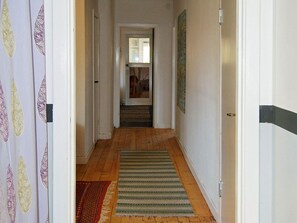 A hallway with wooden flooring, a striped rug, and a door with a black stripe.