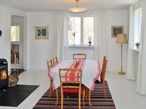 A dining room with a round table, chairs, a fireplace, and a window with curtains. - 4 Star Holiday Home in Vittsjo (Vittsjo)